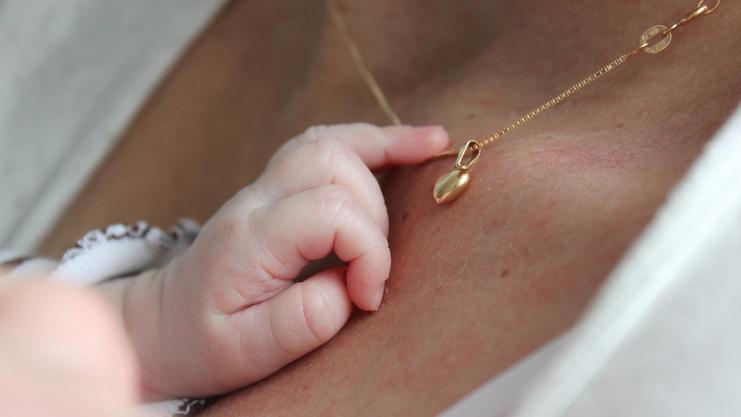 Babyhand greift sanft nach einer goldenen Halskette mit Anhänger auf der Haut einer Person.